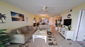 A living room with a beige sofa, a white coffee table, and a patterned rug. There is a TV on a white cabinet, and the room has a ceiling fan. - PALMS OF BAY BEACH-UNIT 1G

EXCEPTIONAL CORNER UNIT ON THE BAY WITH LARGE LANAI (Fort Myers Beach)