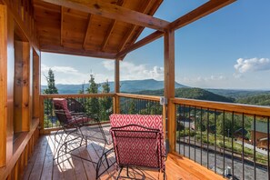 A wooden deck with two chairs and a table, overlooking a mountainous landscape.