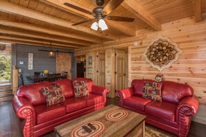 A cozy cabin interior with two red leather sofas, a wooden coffee table, and a ceiling fan.