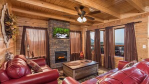 A cozy log cabin interior with a fireplace, leather sofa, and a television mounted on the wall. - The Sweetest Cabin In The Smokies (PIGEON FORGE)