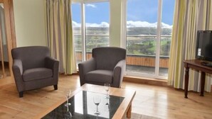 A room with two armchairs, a glass-top coffee table, a television, and large windows with curtains. - Glen View Lodge (Inverness)