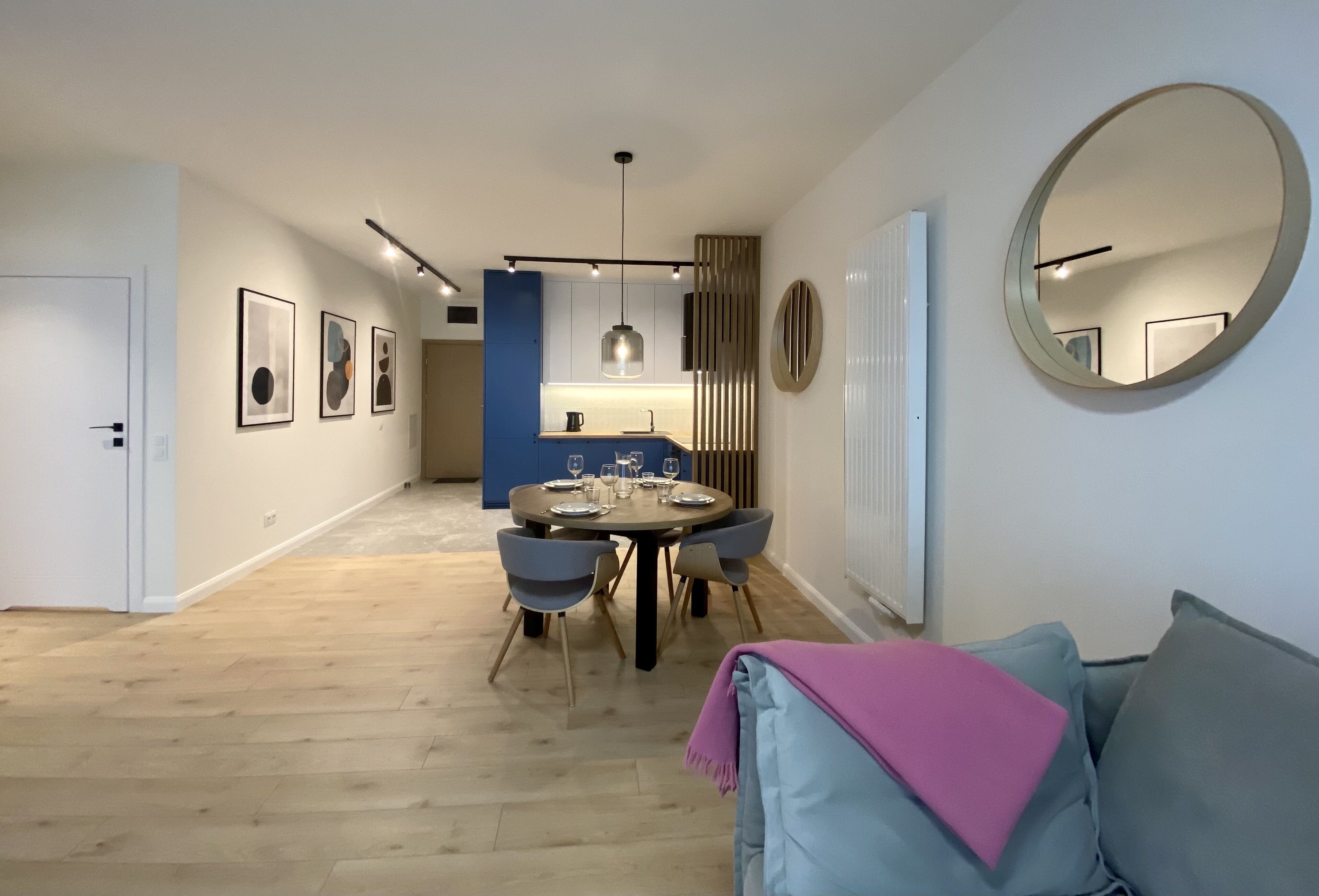 Un salon moderne avec une table à manger ronde, des canapés gris et un grand miroir au mur.