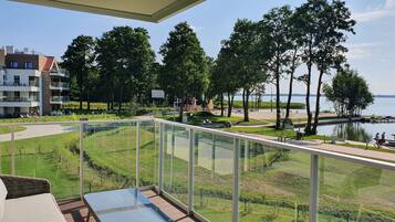 A balcony with a view of a park, a lake, and a building with multiple floors.