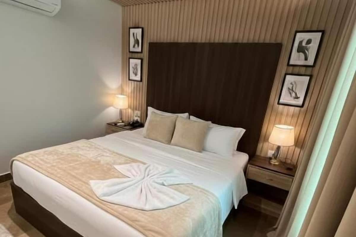 Una habitación de hotel con una cama grande, cabecera de madera, lámparas de noche y aire acondicionado instalado en la pared.