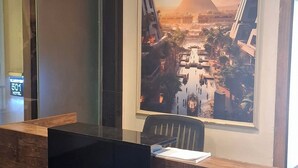 Uma receção com design moderno, um cartaz grande de uma paisagem urbana com uma pirâmide, e uma porta de elevador de vidro.