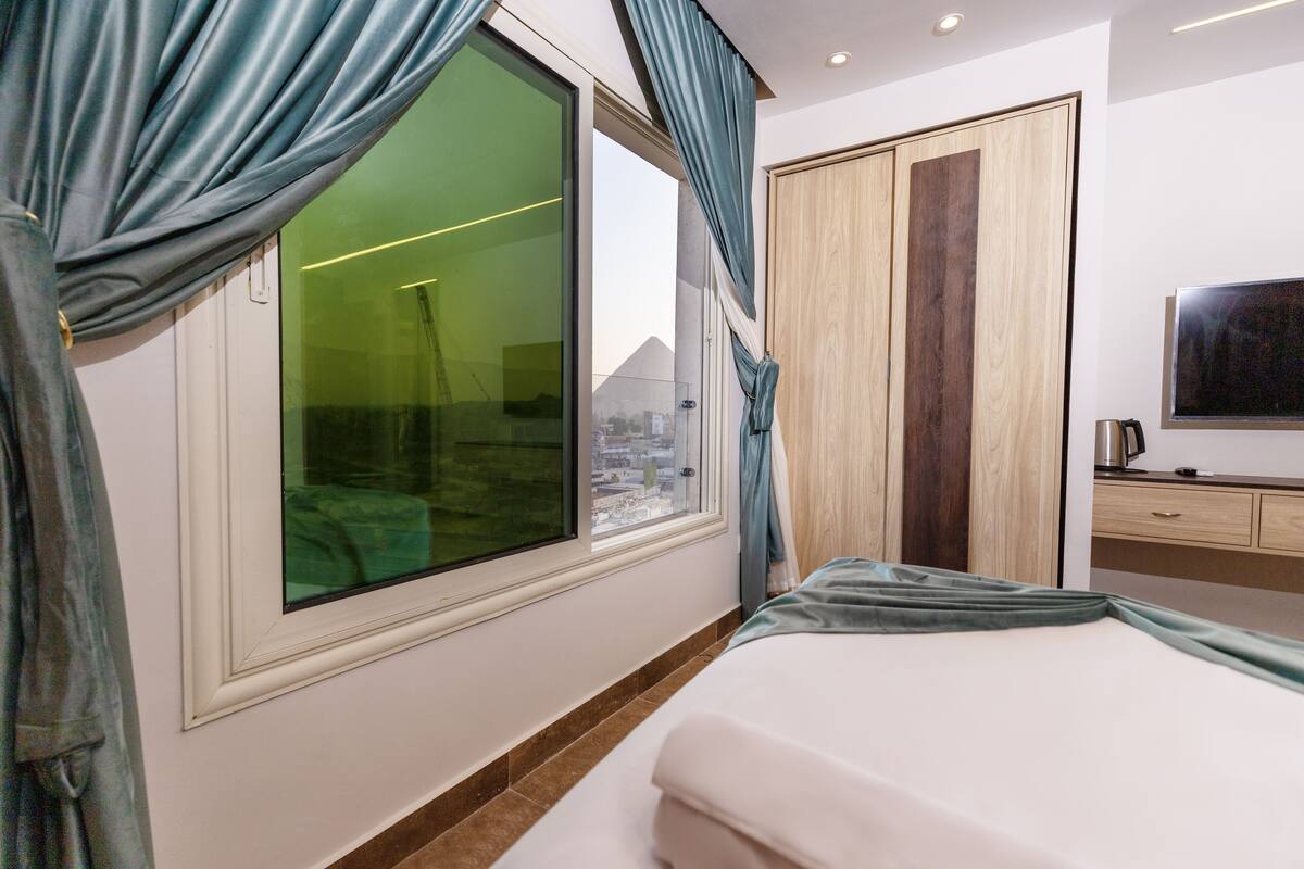 Una habitación de hotel con un ventanal grande, una cama, un armario y un televisor.