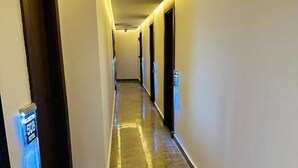Corredor de hotel com piso lustroso, portas em ambos os lados e uma placa na parede esquerda.
