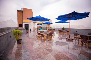 An outdoor terrace with tables and chairs, blue umbrellas, and a potted plant. - Blue Pyramids Eyes Hotel (Giza)