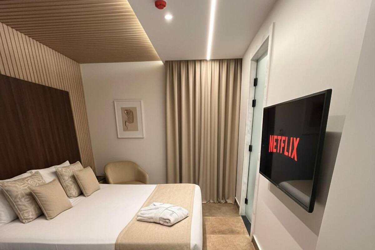 Una habitación de hotel moderna con una cama, una silla, un televisor y una cortina.