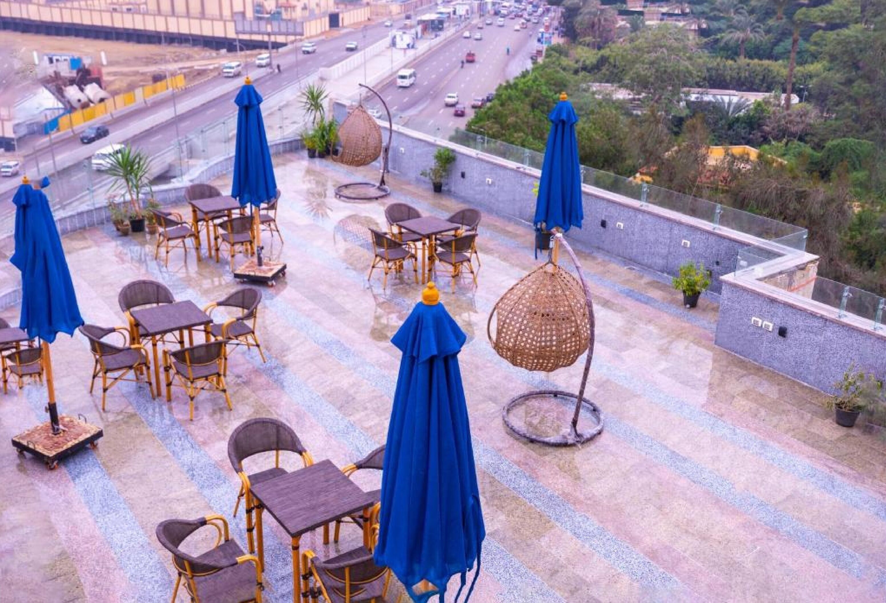 A rooftop terrace with outdoor seating and umbrellas, overlooking a busy highway and greenery.