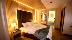 Quarto de hotel moderno com uma cama grande, cabeceira de madeira e mesa de cabeceira com abajur.