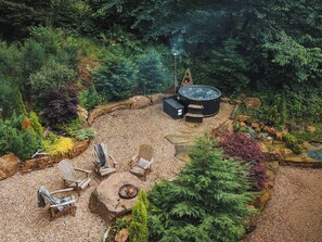 A hot tub surrounded by a garden with seating and a fire pit. - Heilan Roo (Pitlochry)