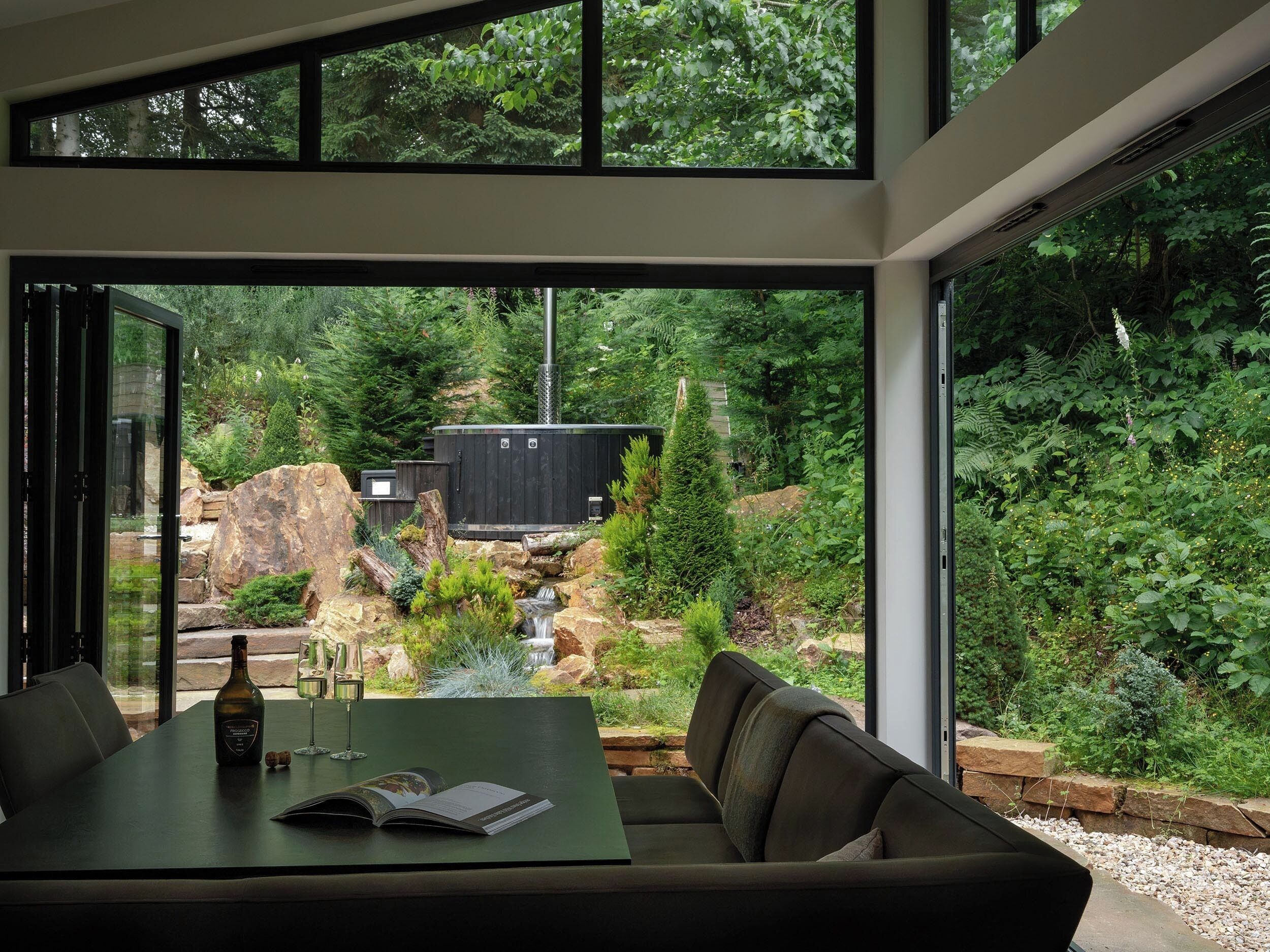 A modern interior with a dining area, a sofa, and a view of a natural outdoor setting.