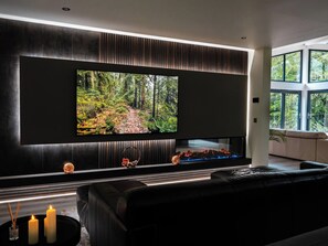 A modern living room with a large flat-screen TV mounted on a dark wall, a black leather sofa, and a fireplace with a glass front. - Heilan Roo (Pitlochry)