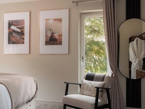 A room with a bed, a chair, a window with curtains, and two framed pictures on the wall.