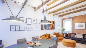 A modern living room with a dining area, featuring exposed wooden beams, a round table with chairs, and a sofa with cushions. - Palazzetto San Stin (Venice)