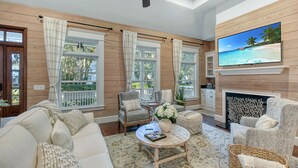 A spacious living room with a fireplace, comfortable seating, and large windows offering a view of the outdoors. - Beautiful 3 bed - 3 bath home located in Village Oaks (Saint Simons Island)
