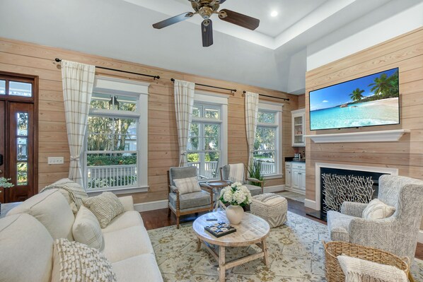 A spacious living room with a fireplace, comfortable seating, and large windows offering a view of the outdoors. - Beautiful 3 bed - 3 bath home located in Village Oaks (Saint Simons Island)