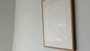 Ein gerahmtes Kunstwerk mit einem gewellten Muster an einer schlichten Wand.