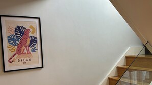 Eine Treppe mit Holzbodenstufen und einem Glasgeländer, die zu einer Zwischenebene führt, auf der ein gerahmtes Kunstwerk an der Wand hängt.