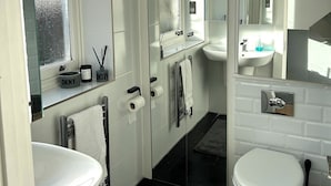 Ein modernes Badezimmer mit Waschbecken, Toilette und großem Spiegel. Zwei Handtuchhalter und ein Fenster mit Milchglas.
