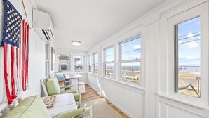 A room with a long window view, a dining area with a table and chairs, and a flag hanging on the wall.