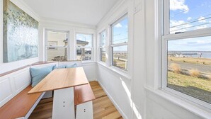 A room with a wooden bench, white walls, and large windows offering a view of a pier and water.