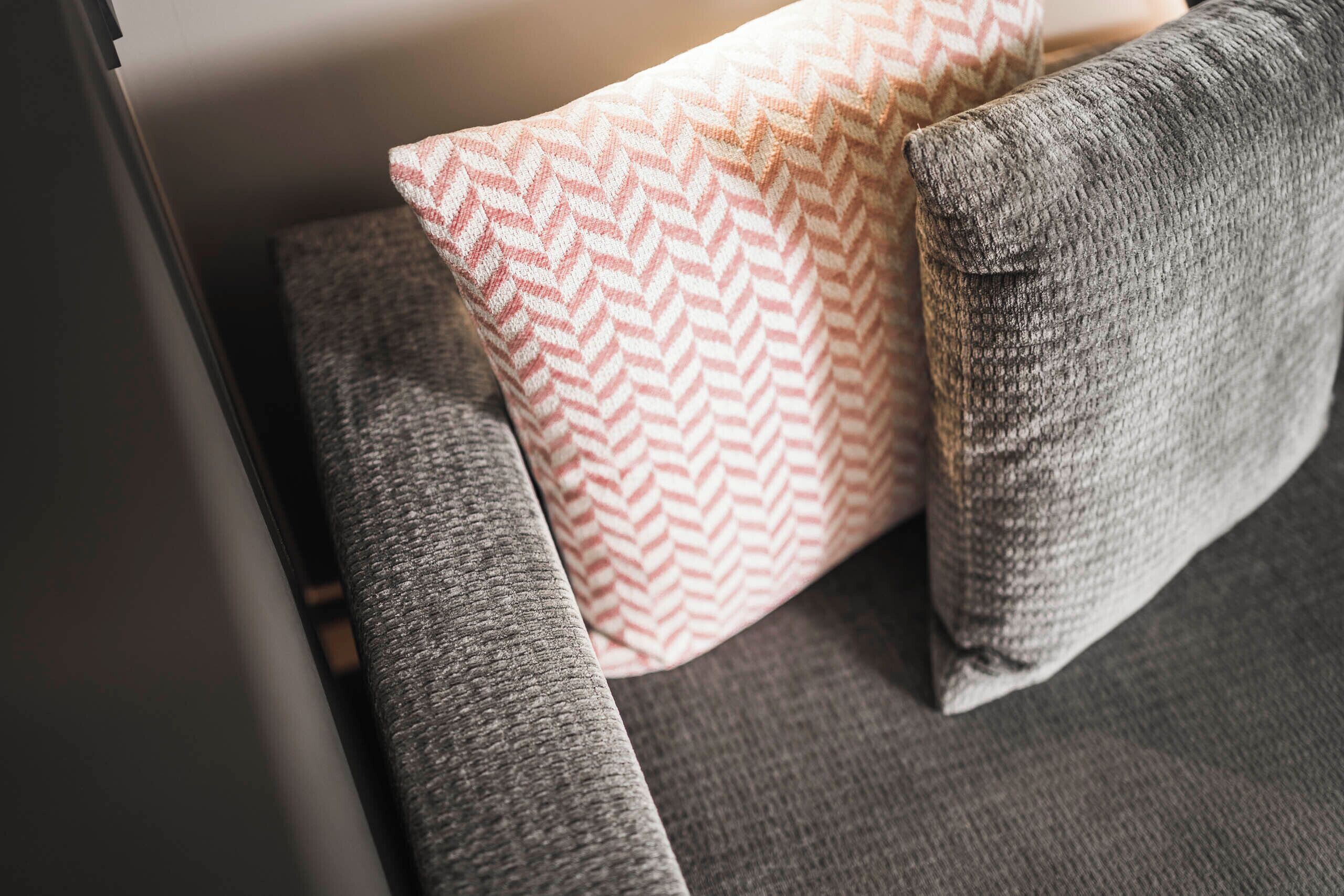 A close-up of a sofa with a grey fabric and a patterned pillow.