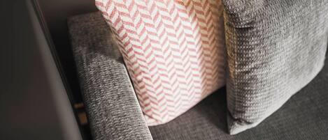 A close-up of a sofa with a grey fabric and a patterned pillow.