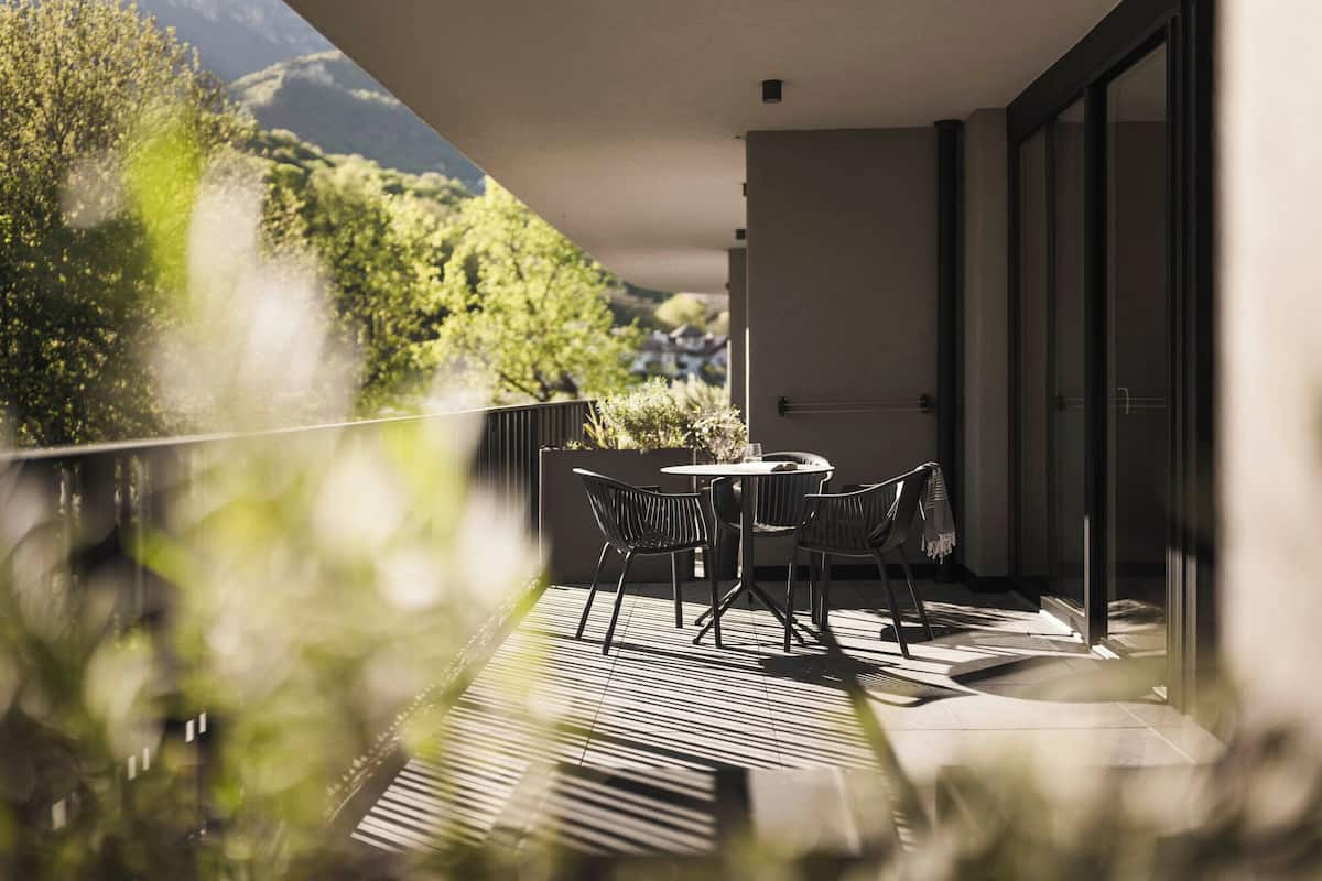 A balcony with a table and chairs, overlooking a mountainous landscape.