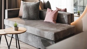 Un salon moderne avec un canapé gris, une table basse ronde et une grande fenêtre avec des rideaux.