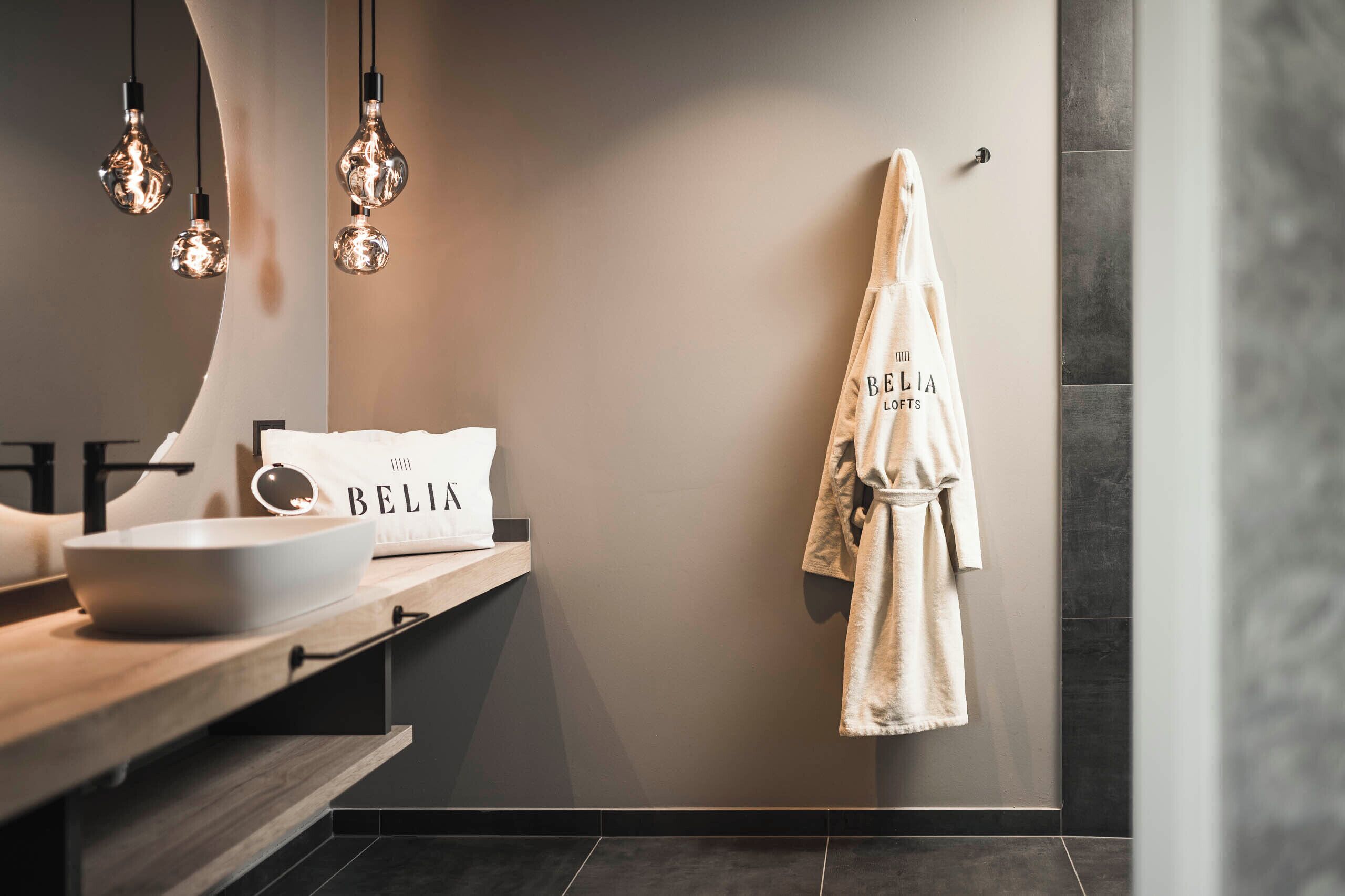 A modern bathroom with a large mirror, a bowl on the counter, and a robe hanging on the wall.