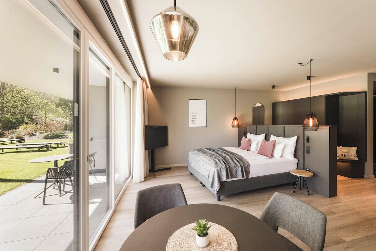 A modern bedroom with a large bed, a dining area, and a view of a garden.