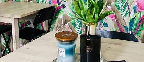 A table with a floral wallpaper background, a candle, and a vase with flowers.