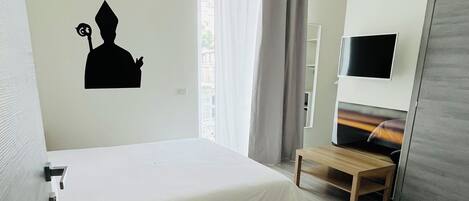A modern hotel room with a bed, a TV, a desk, and a wardrobe.