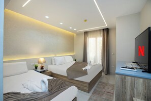 A modern hotel room with two beds, a desk with a television, and a large window with curtains.