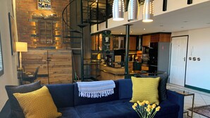 A modern living room with a dark blue sofa, yellow cushions, a glass coffee table, and a vase with yellow flowers. - Artistic Spacious Luxury Loft, a 10 min. walk to V&A Waterfront & fine dining! (Cape Town)