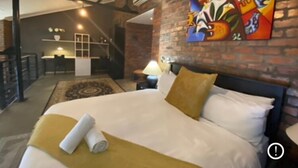 A modern hotel room with a large bed, a painting on the wall, and a dining area in the background. - Artistic Spacious Luxury Loft, a 10 min. walk to V&A Waterfront & fine dining! (Cape Town)
