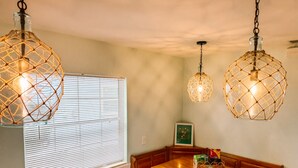 Un comedor con una mesa de madera y un banco, dos lámparas colgantes y una ventana con persianas.