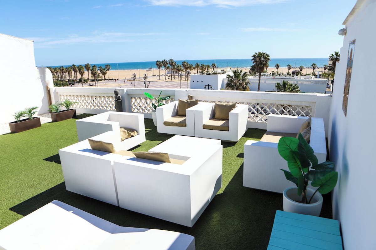 Een terras op het dak met witte tuinmeubels, uitzicht op het strand en palmbomen.