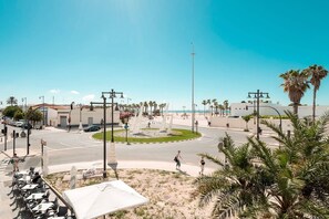 A street view with palm trees, a roundabout, and a building with a red roof. - Valencia Luxury - Malvarrosa Beach (Valencia)