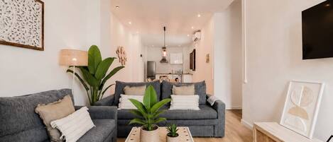 A modern living room with two grey sofas, a coffee table with plants, a TV, and a kitchen in the background.