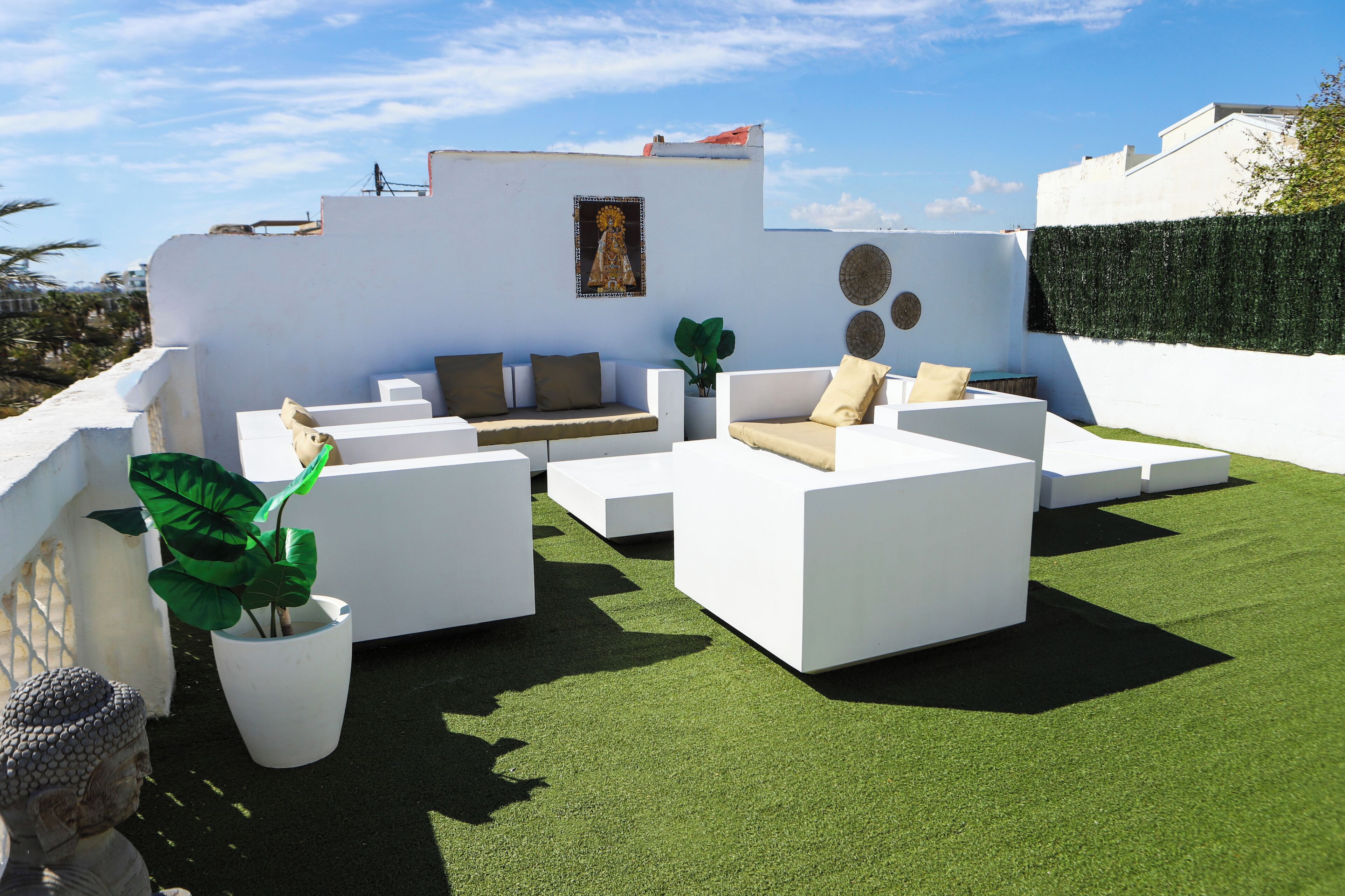 Terraço no telhado com móveis de jardim brancos, uma estátua de Buda e um vaso de plantas.