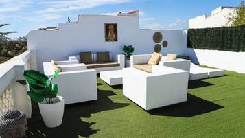Terraço no telhado com móveis de jardim brancos, uma estátua de Buda e um vaso de plantas.