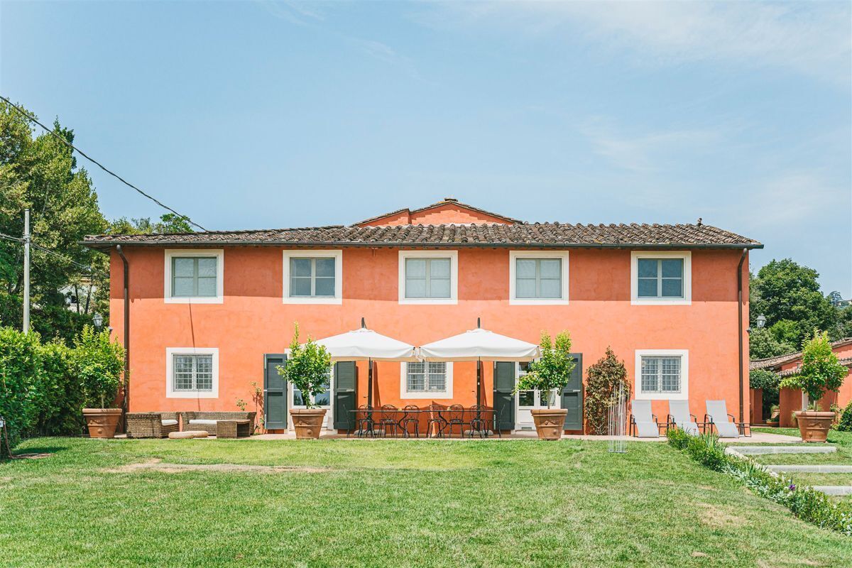 Un edificio a due piani con facciata rossa, tetto in tegole e un patio con mobili da esterno e ombrelloni.