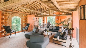 A spacious indoor area with a high wooden ceiling, comfortable seating, and large windows offering a view of greenery. - Villa Anjelica - Ten Bedroom Villa, Sleeps 22 (Lucca)