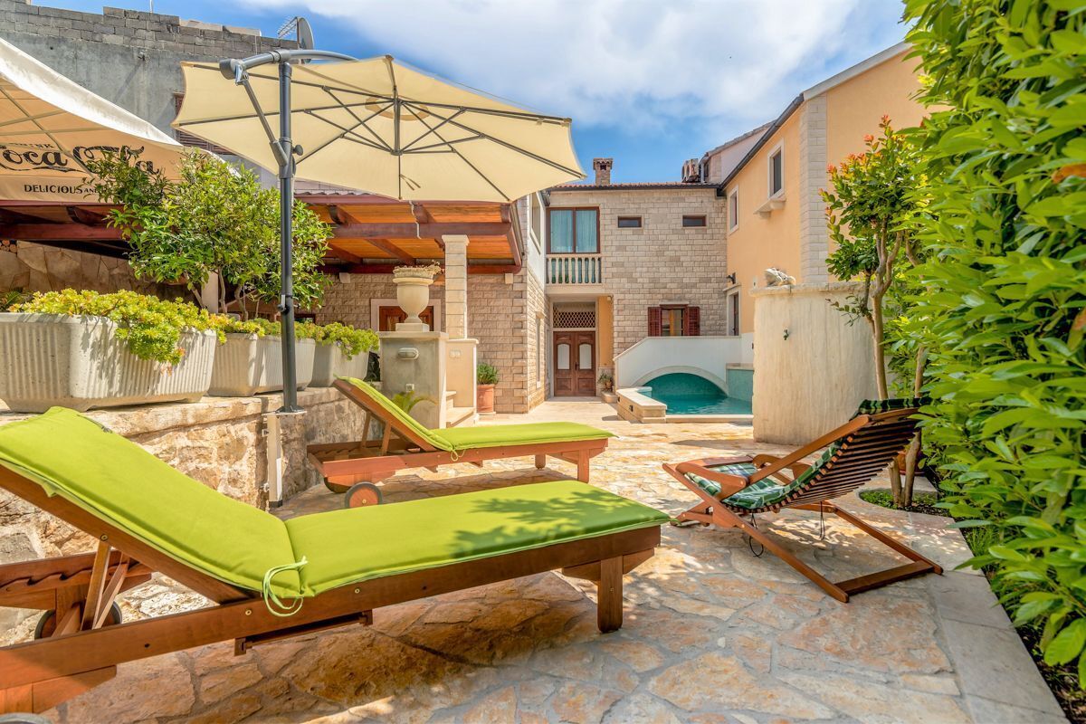 A courtyard with lounge chairs, a pool, and a building with a balcony.