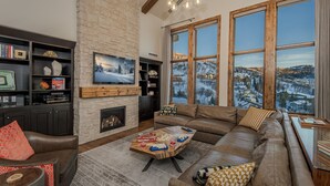 A cozy living room with a fireplace, a large window with a snowy view, a comfortable sofa, and a wooden coffee table.