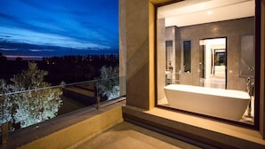 Ein modernes Badezimmer mit freistehender Badewanne, einem großen Spiegel und Blick ins Freie.