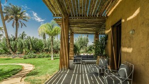 Een terras buiten met een pergola, zithoek en een tuin met palmbomen.